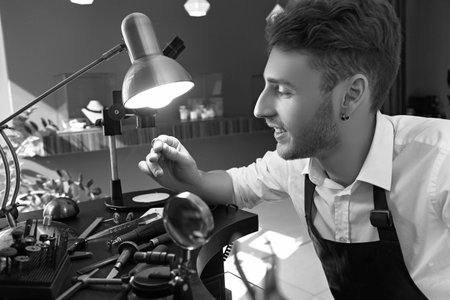 handsome guy jeweler examines a pink gemstone through a magnifying glass in the process of creating...