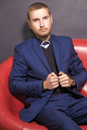 handsome young businessman in a blue suit is sitting on a red couch
の写真素材