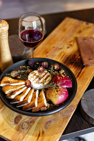 Grilled camembert with baked apple and grapes with slices of bread, served on a black plate on a wooden background in rustic style. Restaurant servingの写真素材