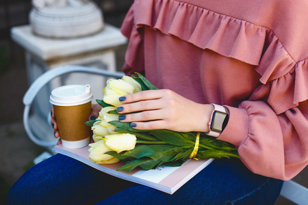 female hands holding a glass with coffee, yellow tulips and a magazineの写真素材