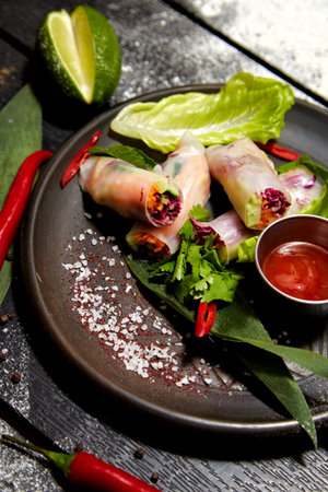 Asian dish on a black plate on a wooden table decorated with lime, pepper, salt, chili and flour....