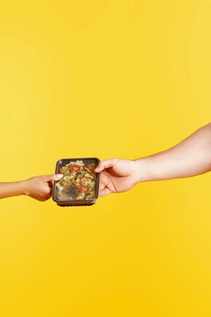 Two hands holding a box of healthy balanced food in the studio on a yellow background. Healthy eating concept, daily dietの写真素材