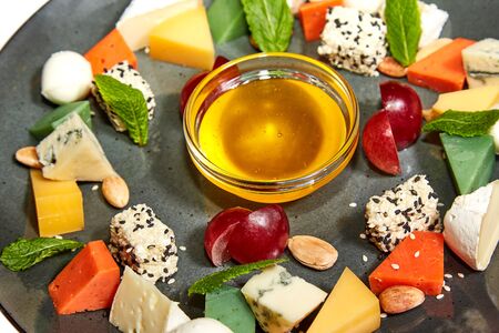 Cheese platter with brie, dorblu, pesto, gouda, nuts, grapes, honey and mint on a large plate on a white background. Restaurant servingの写真素材
