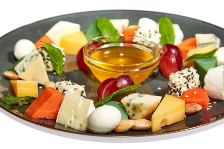 Cheese platter with brie, dorblu, pesto, gouda, nuts, grapes, honey and mint on a large plate on a white background. Restaurant servingの写真素材