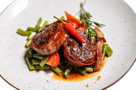 Veal medallions with green beans and chilli pepper on a plate isolated on a white backgroundの写真素材