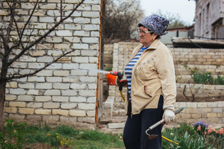 Woman holding garden water hose wearing colorful wellies watering garden