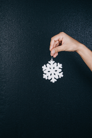 woman hand holding hanging snowflake toy for christmas decoration isolated on black background. new year gift card.の写真素材