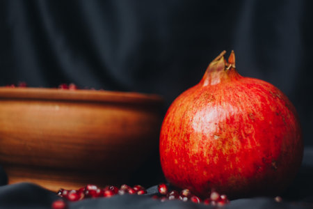pomegranate grains in a brown ceramic bowl on a black fabric background, pomegranate fruit, ceramic...