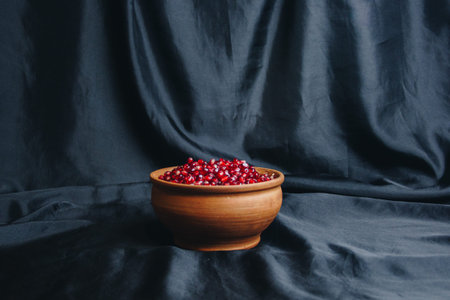 pomegranate grains in a brown ceramic bowl on a black fabric background, pomegranate fruit, ceramic jug, ceramic plate, isolated still life close upの写真素材