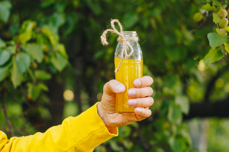 man holds in his hand bottle of homemade lemonade on the background of trees in the park and green grass. sunny day, summer. closeup healthy food fresh. cropped imageの写真素材