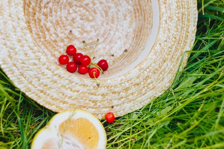 cherry and cuted citrus fruits with straw hat lying on the grass outdoors. Picnic on nature in the park close up healthy food, diet, personal care. sunny dayの写真素材