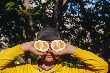 a man in a yellow hoodie and blue panama is holding two halves of a yellow citrus cut in half before...