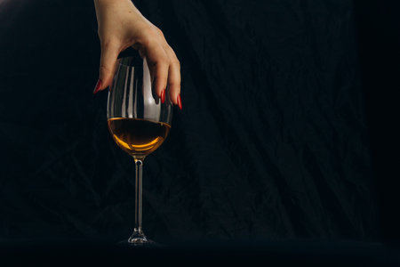 cropped female hand holding a glass of white wine on a black background. rest, holiday, party....