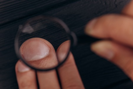 men's hands on a rustic black desk holding a magnifying glass. fingerprint examination. palm closeupの写真素材