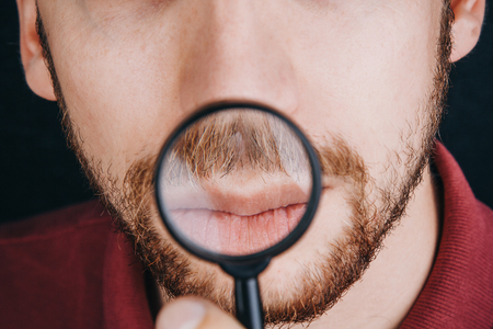 beard under a magnifying glass. hairline on a man's face close up. portrait of a guy with a mustache.の写真素材