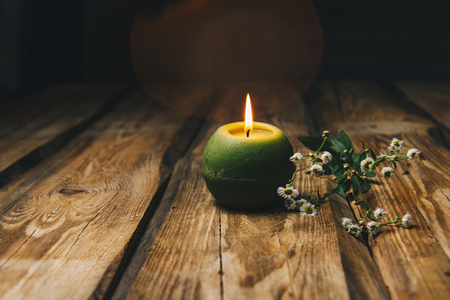 single green ball-shaped candle with a dry flower burning on a rustic wooden table close-up.の写真素材