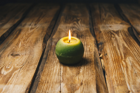 lonely green ball-shaped candle burns on a rustic wooden table close-up.の写真素材