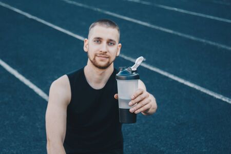 muscular slender man in training at the stadium drinks water from a sports shaker. recreation sports. athletic exercising.の写真素材