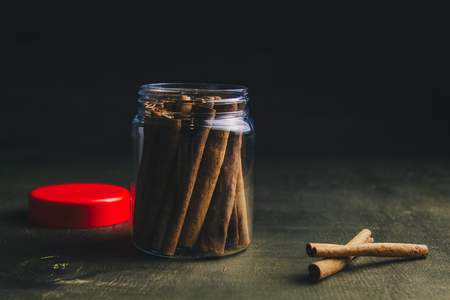 whole sticks of fragrant cinnamon are tightly packed in a transparent jar with a red lid on a wooden rural table. copyspace. composition of seasoning and flavoring aromatic spice.の写真素材
