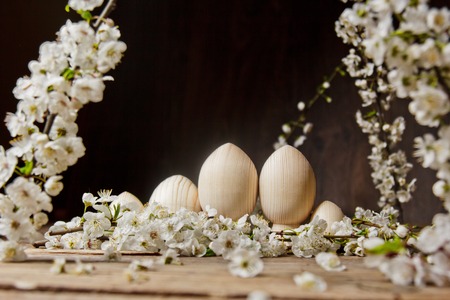 wooden easter eggs among flowering cherry branches on a rustic table. symbolic composition of the spring holiday for a gift card. copy space. close up. petals of white flowers. the rebirth of nature.の写真素材