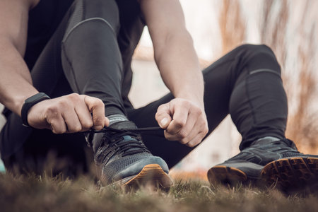 A young man in black clothes is tying the laces on the sneakers close up. fitness athlete sitting on...