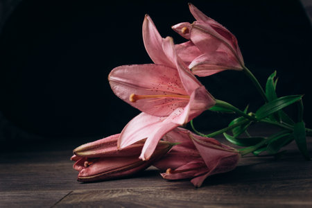 bouquet of pink lily flowers in the rays of light on a black background on a wooden rustic table....