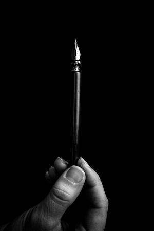 female hand elegantly holding an ink pen with a metal tip close-up on a black background. classic fountain pen isolated macro black and white. copy space. vertical.の写真素材