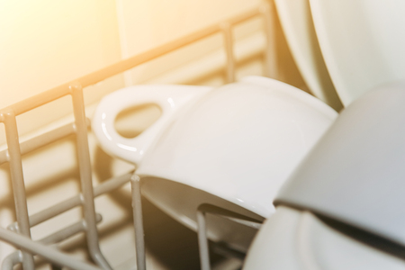 open dishwasher close up clogged with clean washed dishes. dry cutlery closeup. spoons forks. mugs, plates. household appliances in the kitchen.の写真素材