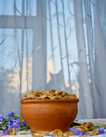 falling sugar cornflakes in a ceramic bowl close-up top view. light breakfast scattered on the table...