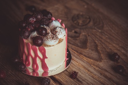 festive cake with the fruits of cherry on a rustic wooden table on a dark background. close up copy space. vintage pattern on dessert tartlet. birthday holiday.の写真素材
