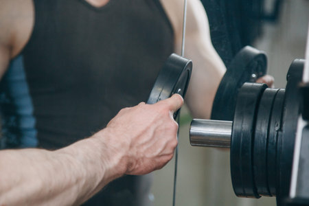 an athlete with big hands adds weight by the metal disks to the training apparatus in the training...