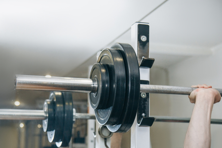 athlete with big hands holding a barbell bar in the training center. training tools in the gym close-up.の写真素材