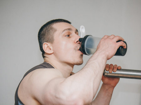 the athlete drinks water from a shaker in the training center. rest between exercises in the gym.