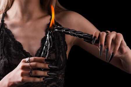 Female hands with long nails hold burning candles on a black isolated background. concept of witchcraft witchcraft on halloween. silver rings on the fingers. sexy slim girl in lace bra.の写真素材