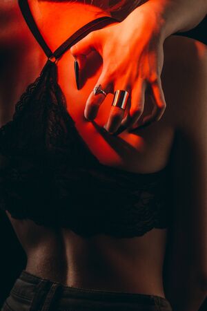 Female hands with long nails hug a thin tender defenseless female body on an isolated black background. self-hatred concept. silver rings on the fingers. sexy slim girl in lace bra.の写真素材