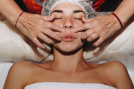 spa specialist is doing facial massage to a young girl in a medical cap. beauty treatments close-up.の写真素材
