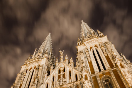 Catholic church on a background of a strange sky. Gothic building with sharp spiers against the backdrop of scary clouds at night illuminated by a lantern.の写真素材