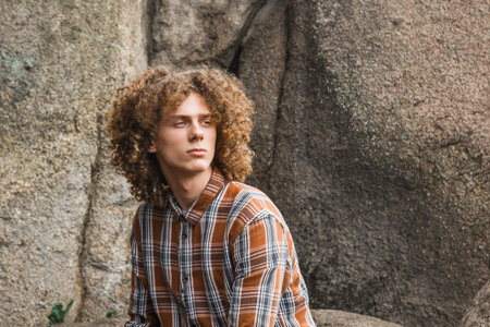 portrait of a young curly-haired guy among the stones on the street. student and young traveler...