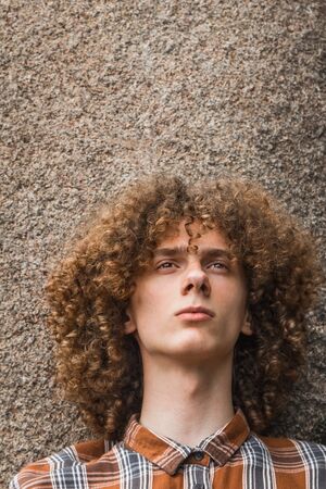 portrait of a young curly-haired guy among the stones on the street. student and young traveler concept.の写真素材