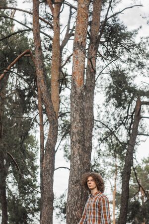 portrait of a young curly-haired guy in a summer park on the street. student and young traveler concept.の写真素材