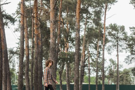 portrait of a young curly-haired guy in a summer park on the street. student and young traveler concept.の写真素材