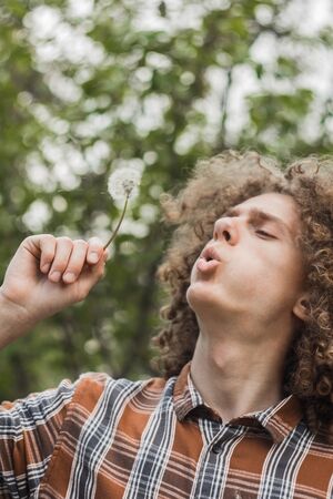 portrait of a young curly-haired guy in a summer park on the street. student and young traveler concept.の写真素材