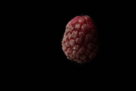 one berry of red raspberries lies isolated on a black background top view close-up. sweet summer berries close-up.の写真素材