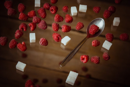 berries of red raspberries with a teaspoon and cubes of refined sugar lie on a wooden rustic table top view.の写真素材