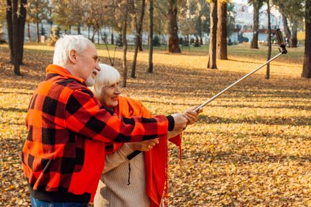 Positive mature couple showing tongues, laughing and fooling around while taking selfie pictures in the parkの写真素材