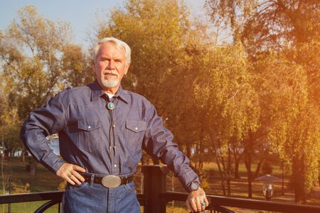 Dreamy grandfather expressing positive emotions. Portrait of a happy old handsome man in the park in autumnの写真素材