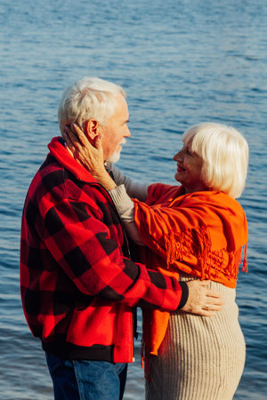 cheerful senior citizens woman and man are standing and hugging on the lake, against the background...