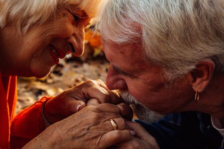 Close up portrait of a happy old man kissing his wife's hands. In the park in autumn foliage a happy couple is restingの写真素材