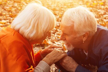 Close up portrait of a happy old man kissing his wife's hands. In the park in autumn foliage a happy couple is restingの写真素材