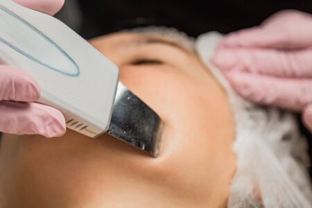 close-up. Ultrasonic face cleaning. Modern equipment. Beautician does cosmetic procedure on woman faceの写真素材